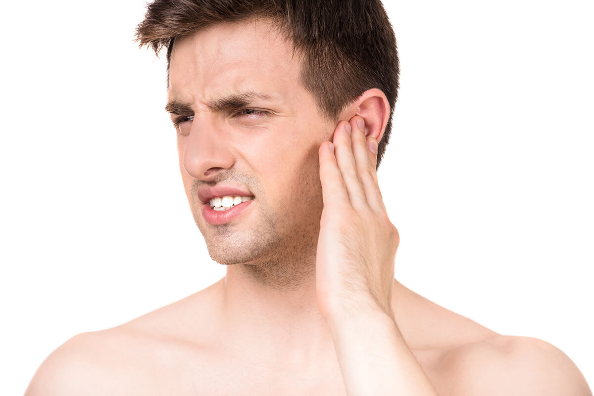 Zapalenie ucha - młody mężczyzna trzyma się za ucho.