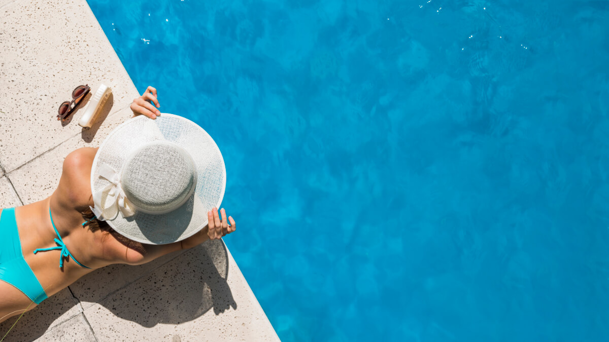 Kobieta opala się nad basenem. Ochrona przed słońcem - jak zabezpieczyć miejsca wrażliwe na skórze